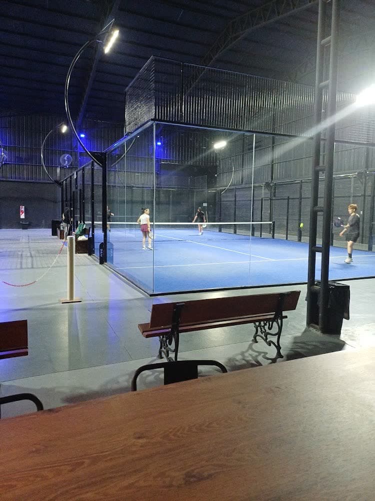 Cancha de cristal con césped azul y un banco al costado